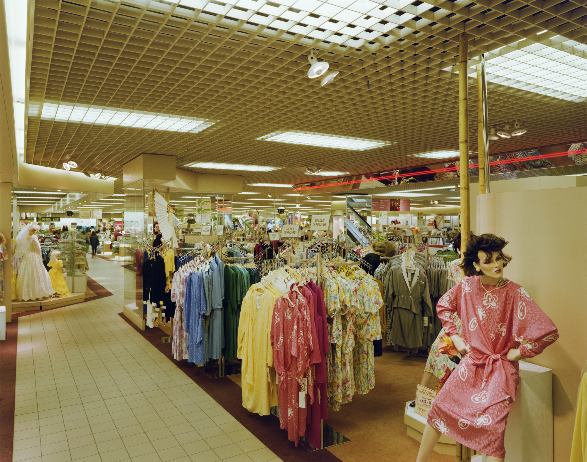 Colour photograph showing the womenswear department in the Allders store at Eastgate Shopping Centre. Colourful clothing is hanging on display stands and a mannequin in the foreground is modelling a pink dress.