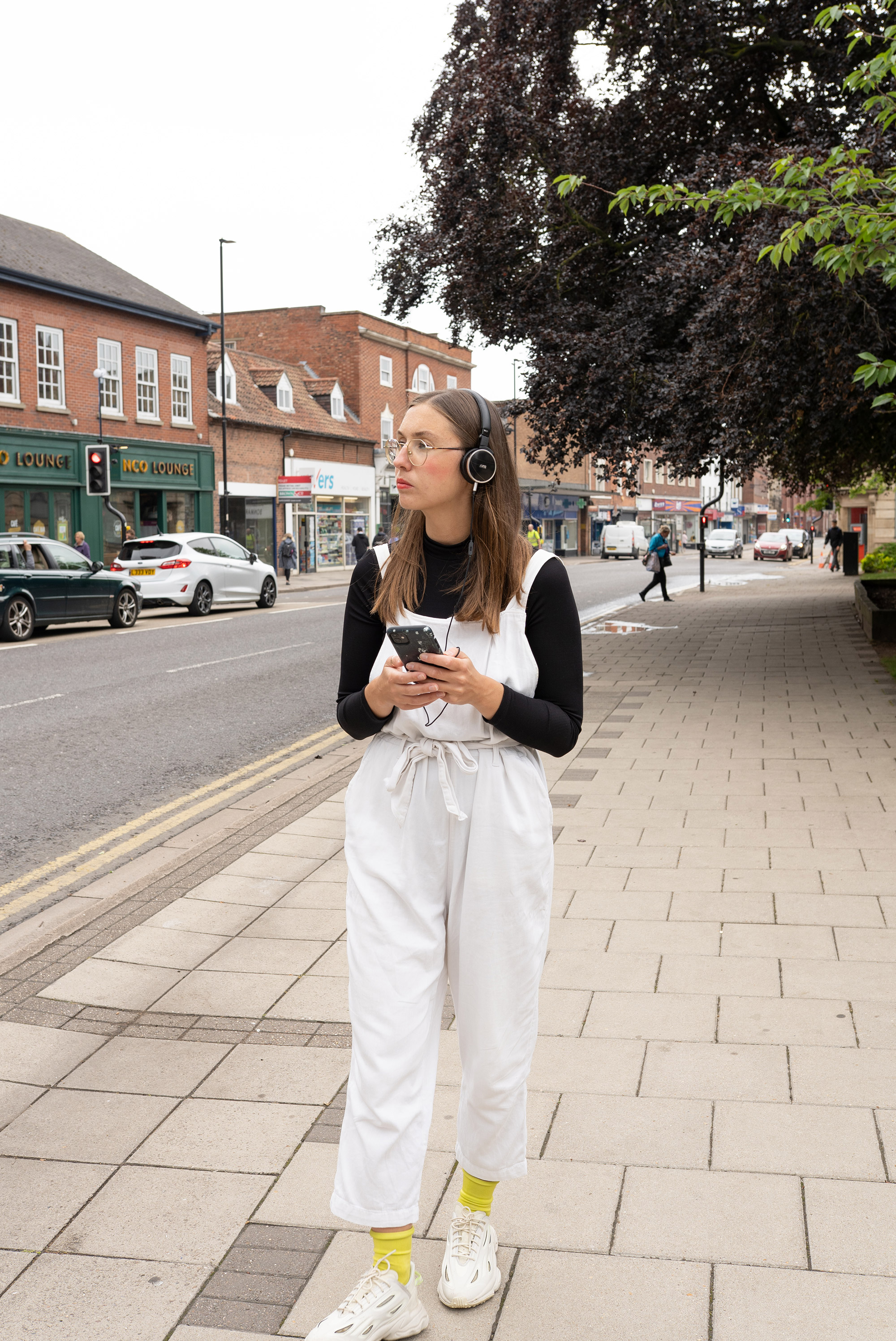 Woman walking down a high street listening to something on headphones.