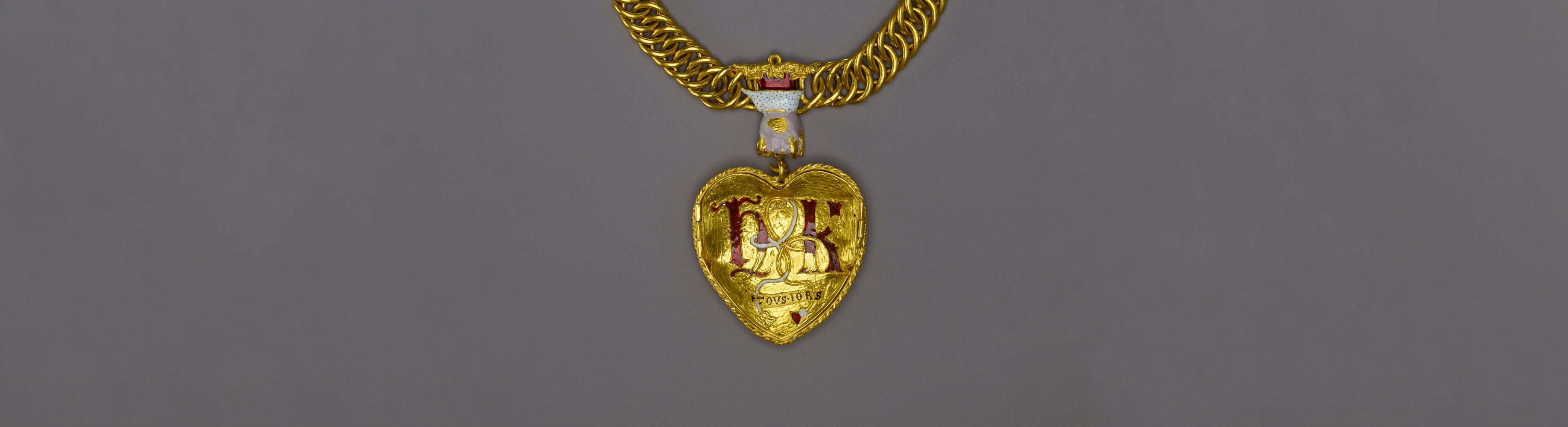 A large, heart-shaped gold pendant on a thick gold chain, suspended from a hand-shaped ornamentation, and detailed with a rose and pomegranate. 