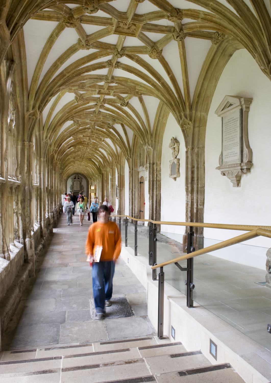 Interior view of people walking along one of the cloisters of Wells Cathedral