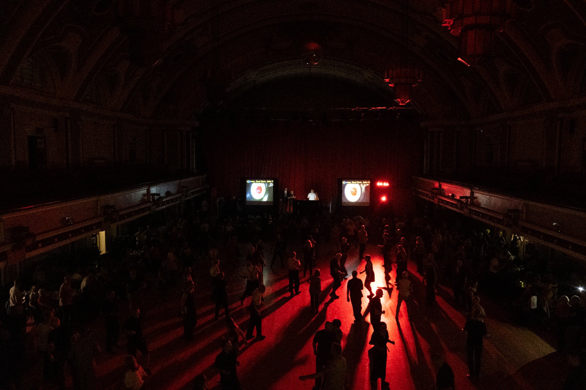 In a darkened room, red light illuminates dozens of people dancing.