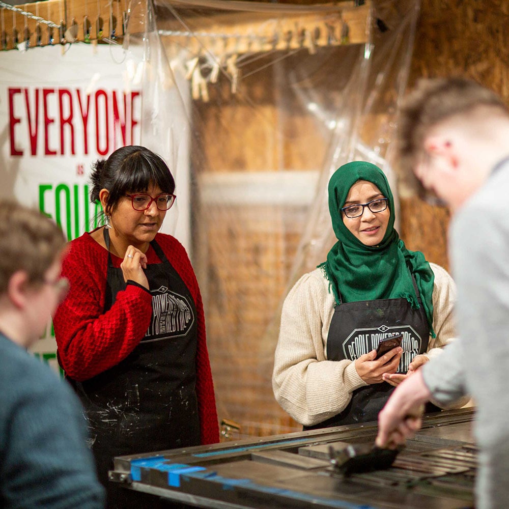 Young people wearing "People-powered press" aprons set letters on a large wooden printing dye