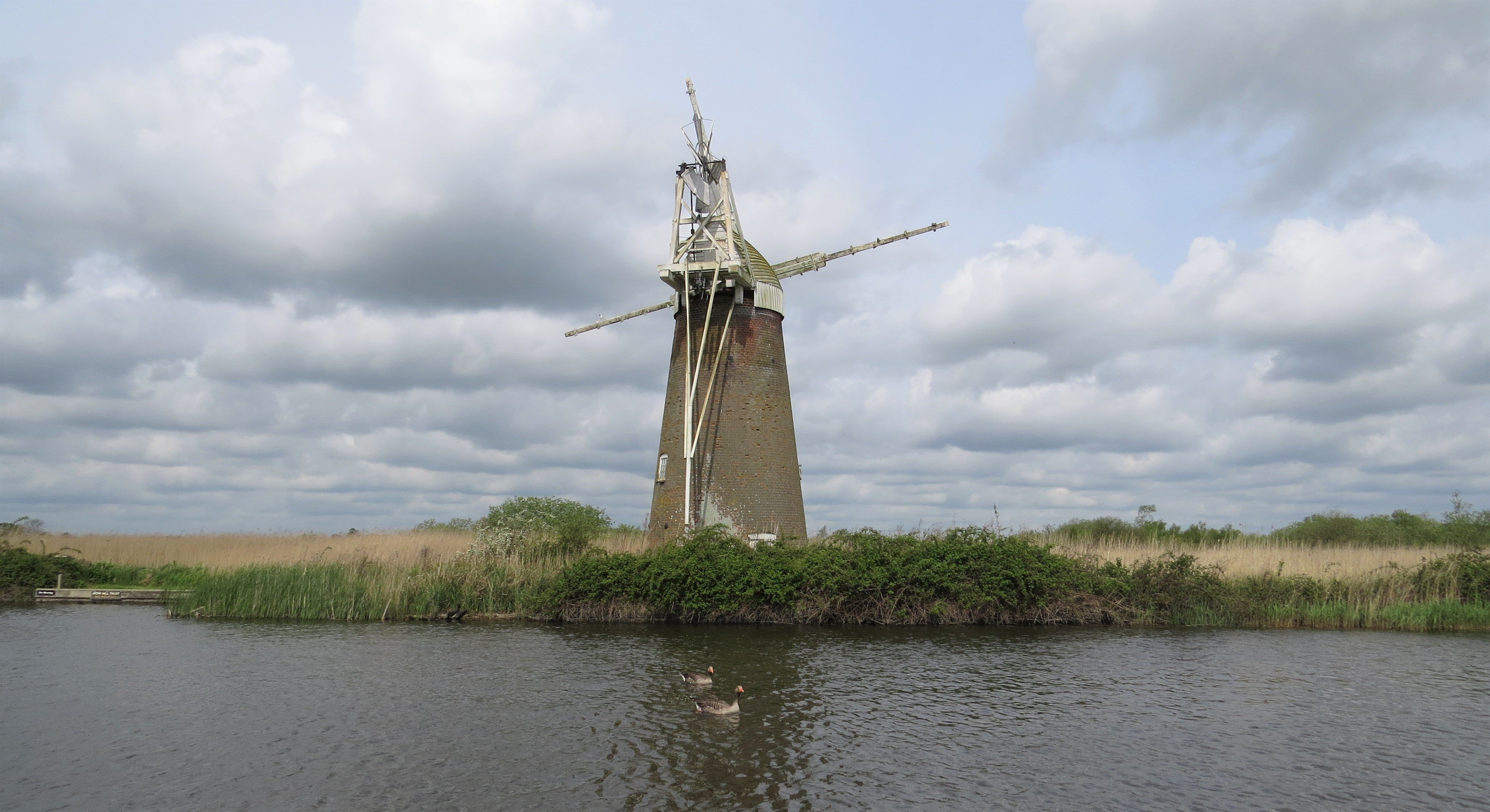 External shot of a windpump with a river in the foreground.