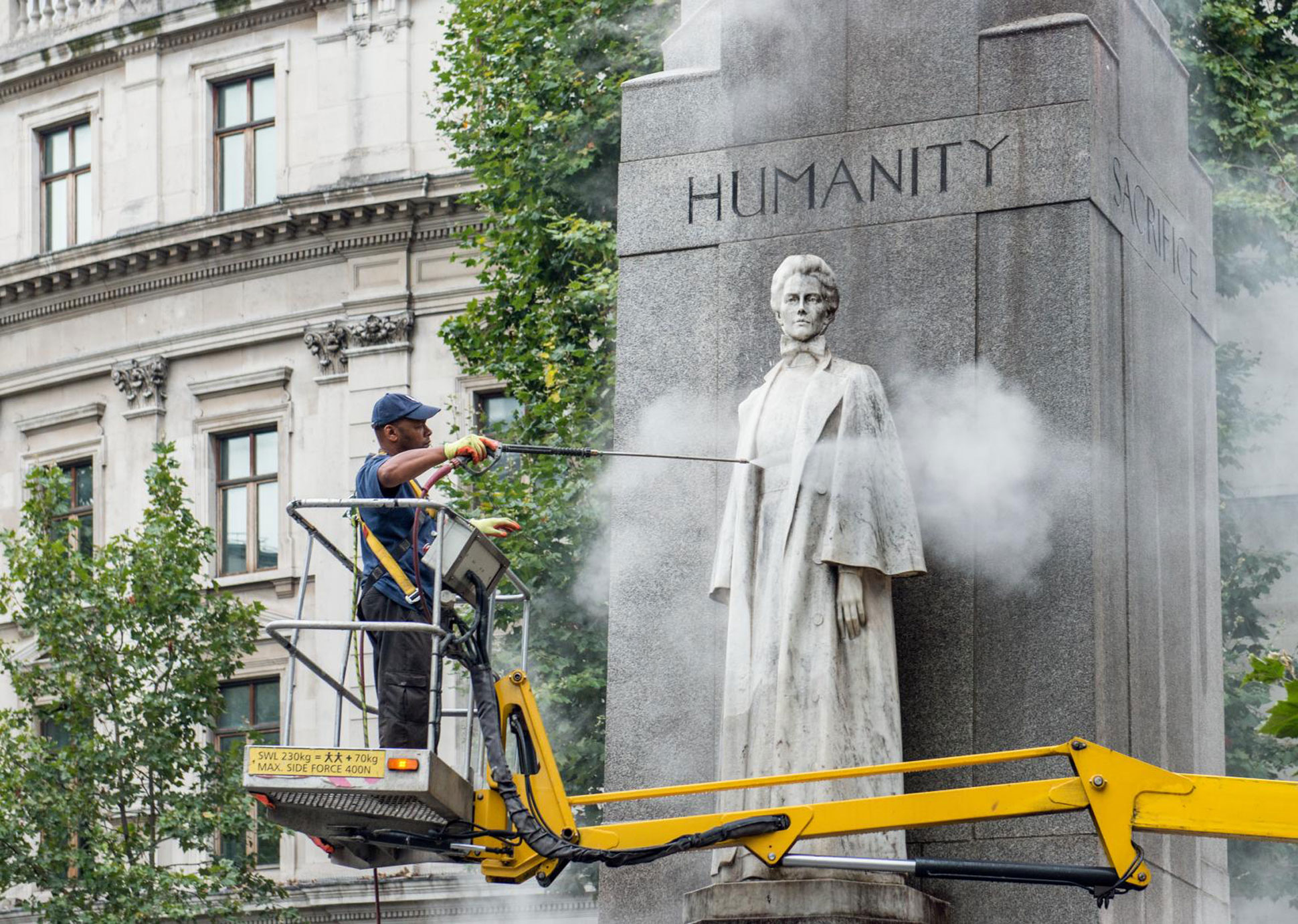 A specialist contractor standing on a cherry picker and cleaning a grey stone memorial to Edith Cavell using a jet wash.