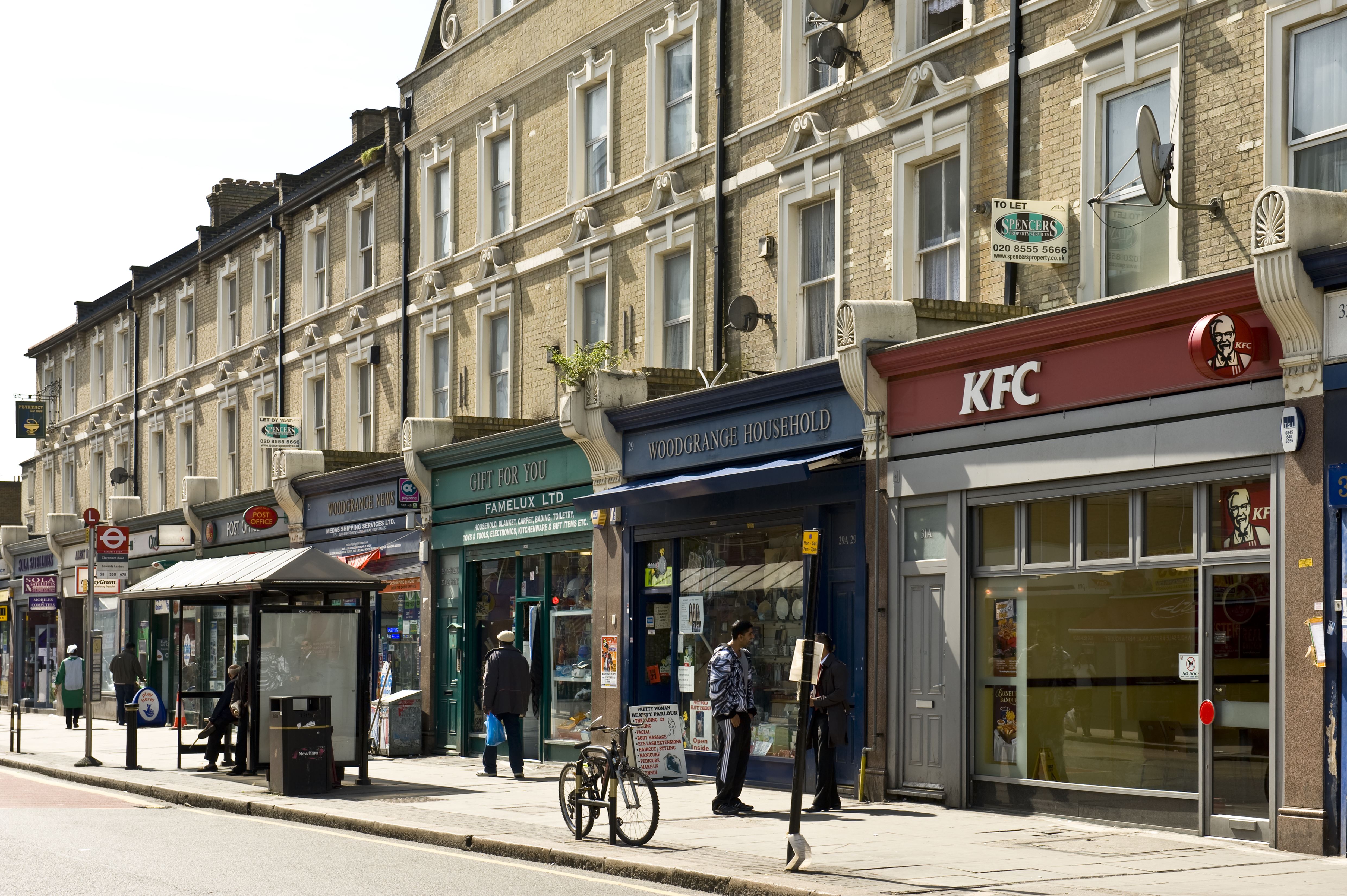 Exteriors of Woodgrange Road commercial premises as shoppers make their way along the sunny street.