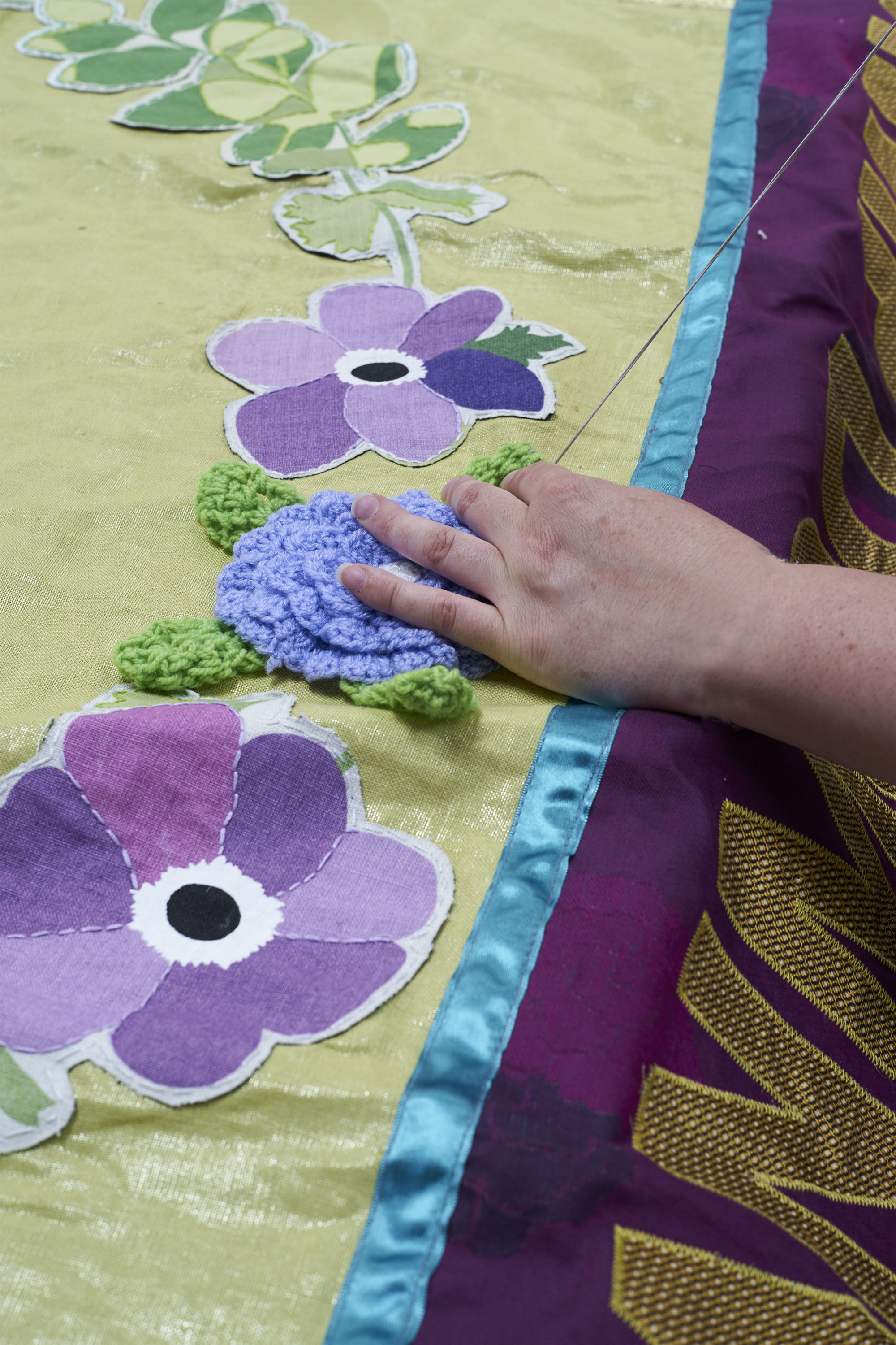 A pair of hands sews a crocheted poppy on a yellow piece of cloth.