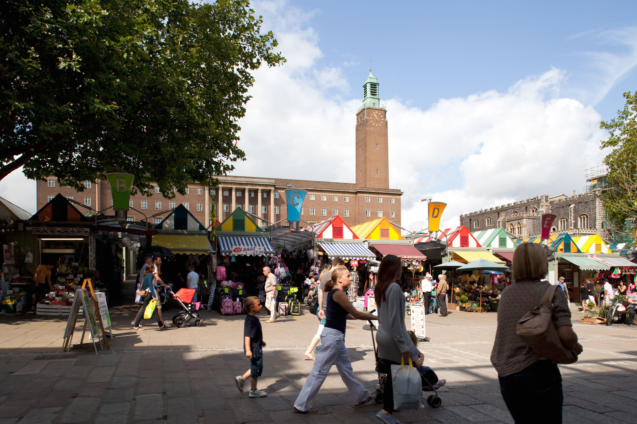 People around market stalls with a large civic building in the background.