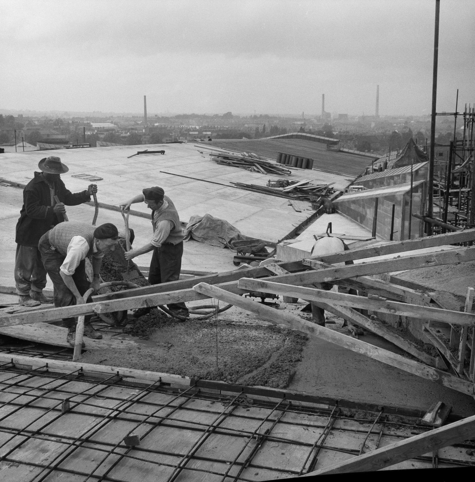 Black and white photo of three men pouring concrete. They aren't wearing any hard hats or high-vis clothing.