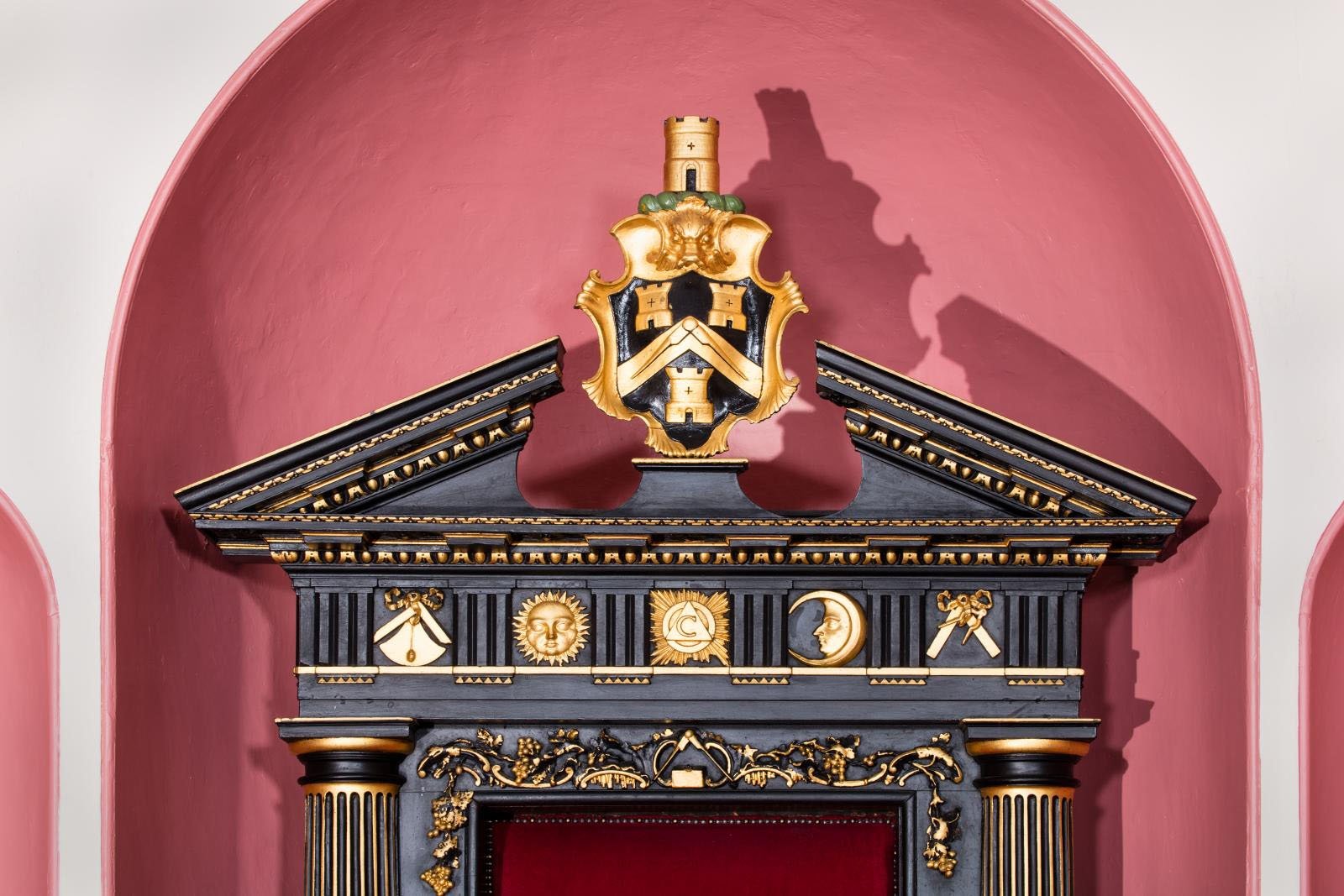 Coat of arms on top of a throne with masonic symbols underneath. Wood is black with gold leaf decoration.