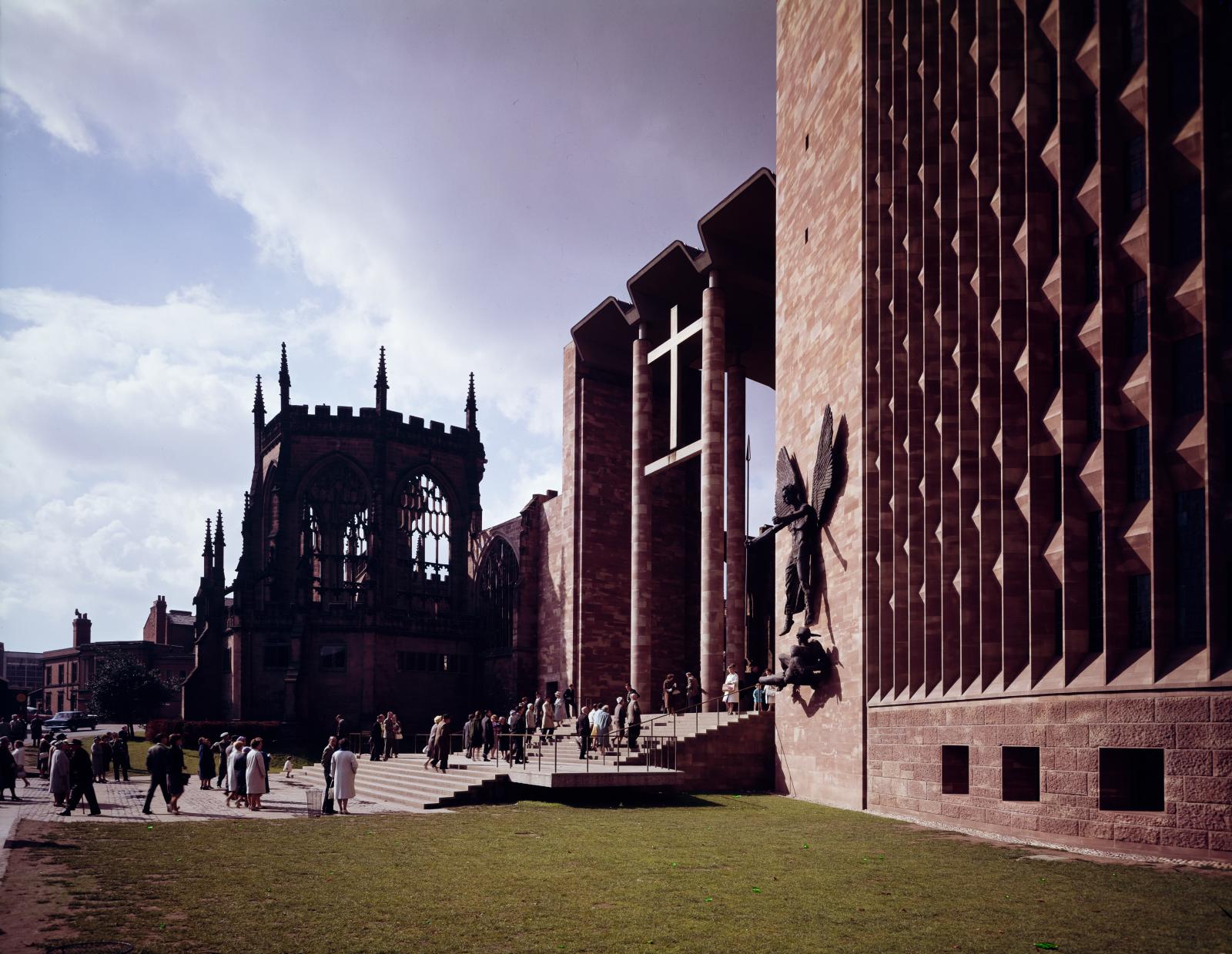 Colour photo of the porch of Coventry Cathedral with the ruins of the old cathedral behind and to the left.