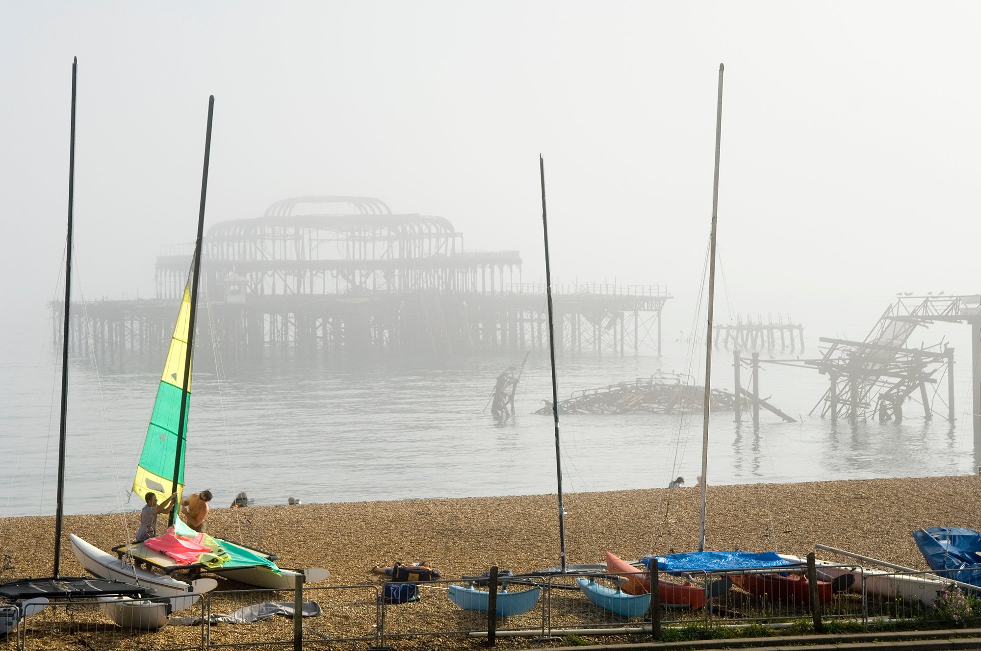 Image of the burnt out West Pier in Brighton, showing the pier in the background with the beach and masts of boats in the foreground.