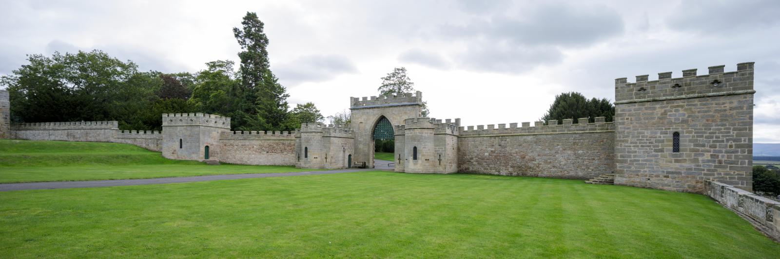Crenellated castle wall and gateway with expansive lawns in foreground.