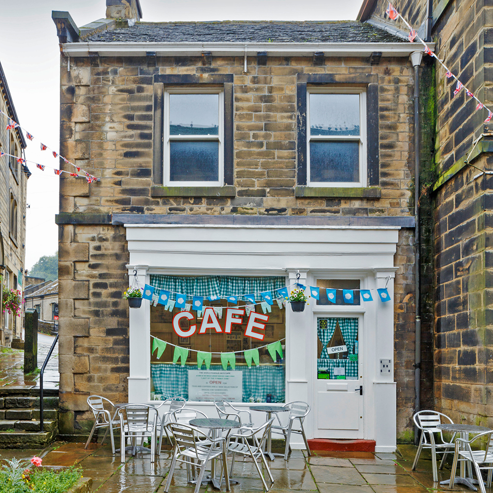 Rainy exterior of an urban cafe building with bunting and steel table sets outside. 