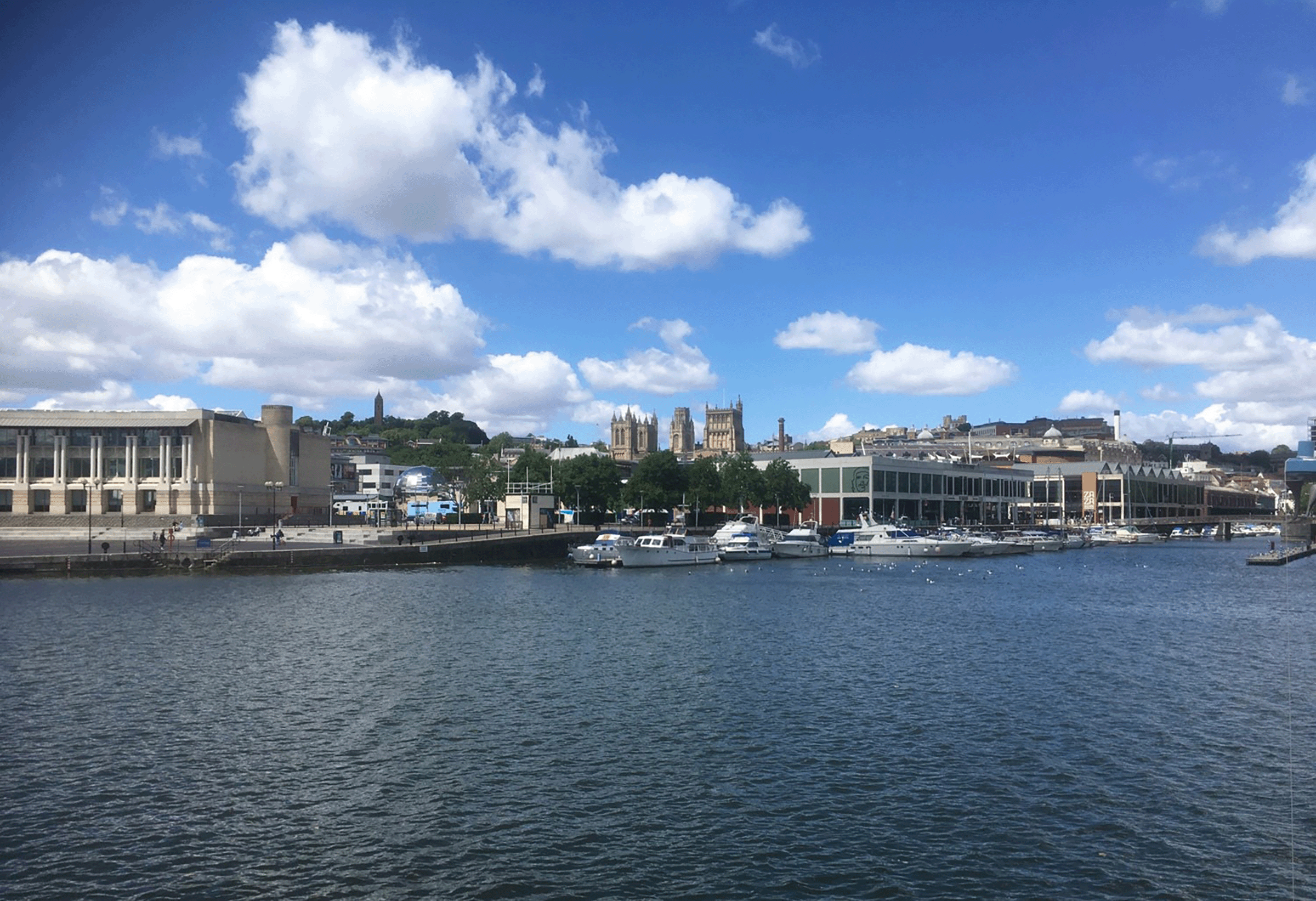 A view across the river towards Bristol's harbourside buildings. The towers of Bristol Cathedral can be seen rising above in the middle ground.