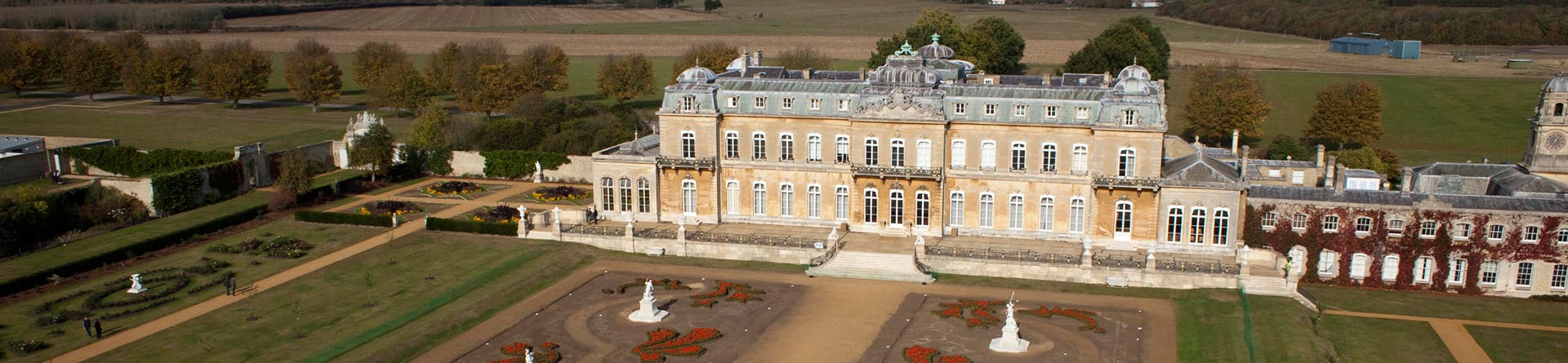 Low level, colour aerial photograph showing a grand country house and gardens with formal planting and statues