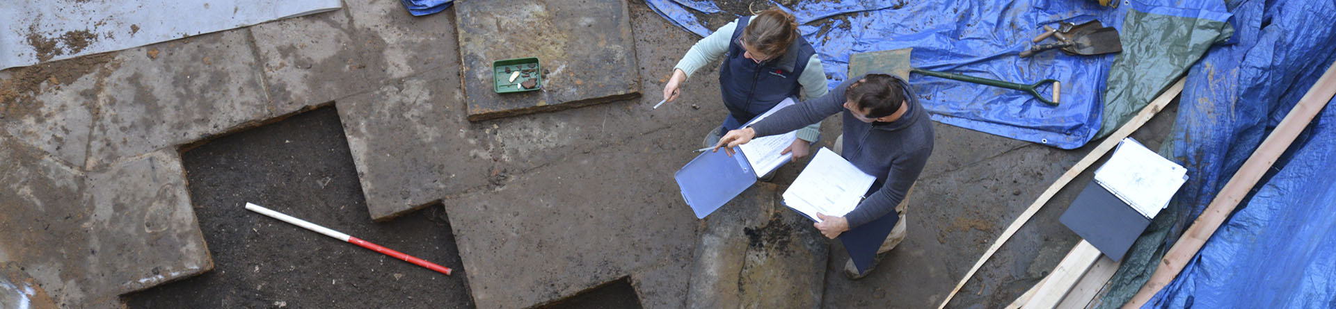 A view looking down into the interior of the tower, showing two archaeologists discussing and recording the trench in front of them.