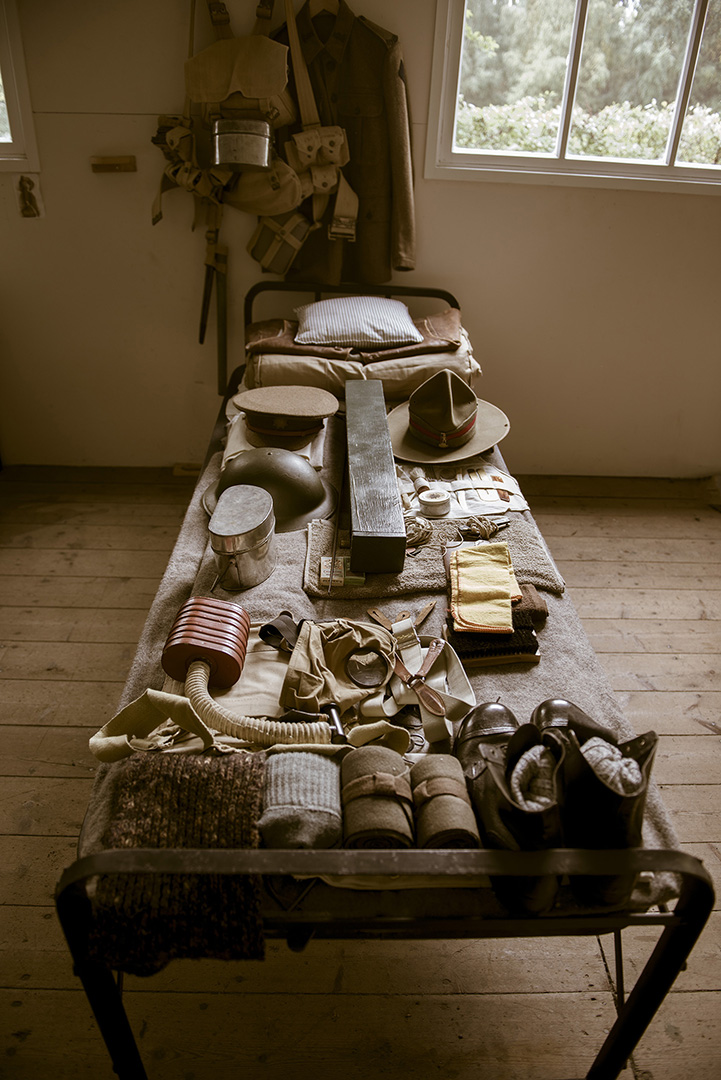 Colour photograph showing a bed with kit on top including several hats, boots and packs.