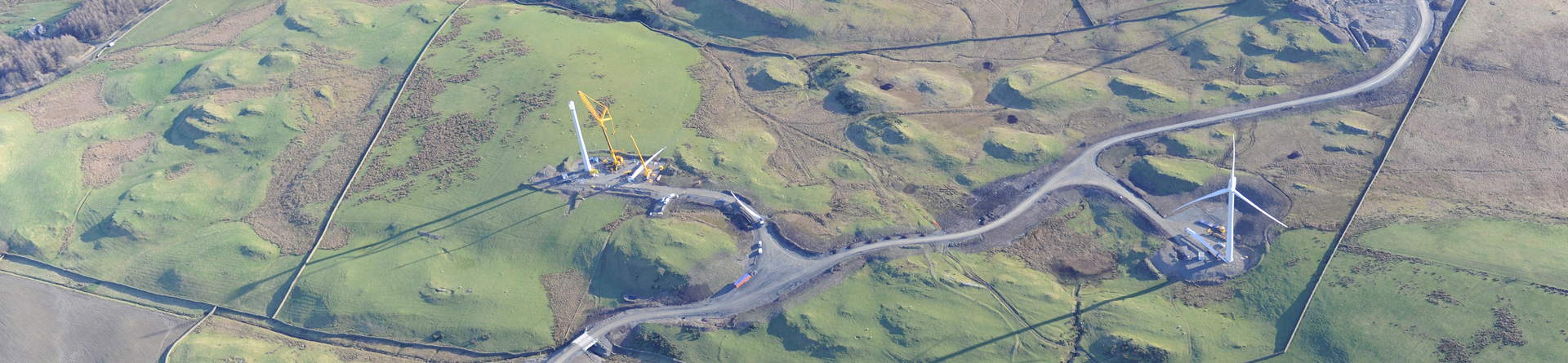 Colour aerial photograph showing one complete wind turbine and one under construction with the cranes and construction road
