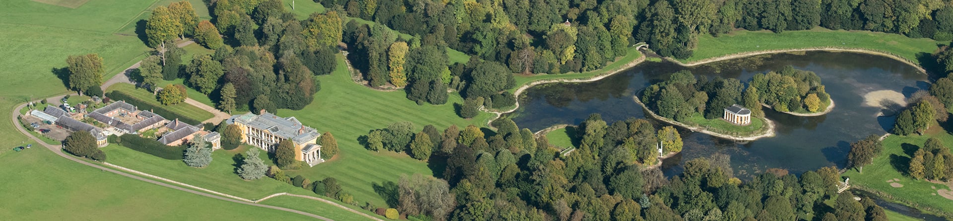 Colour aerial photograph of a country house with landscaped gardens and a lake with some islands, one of which hosts a temple
