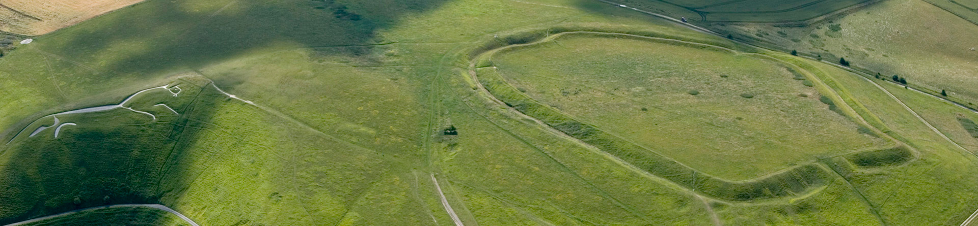 Colour aerial photograph showing a large banked earth enclosure to the right and a white chalk stylised figure of a horse left.