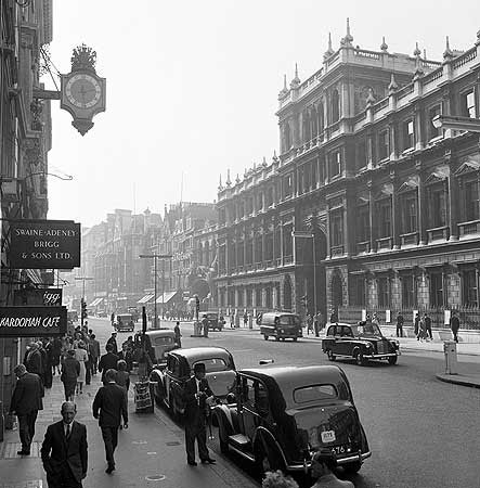 A view of Piccadilly in the City of Westminster, looking west over traffic, with the grand facade of the forecourt buildings to Burlington House to the right. Burlington House itself houses the Royal Academy of Arts where deaf artist Thomas Arrowsmith studied and exhibited. Photograph by John Gay, circa 1950-60.