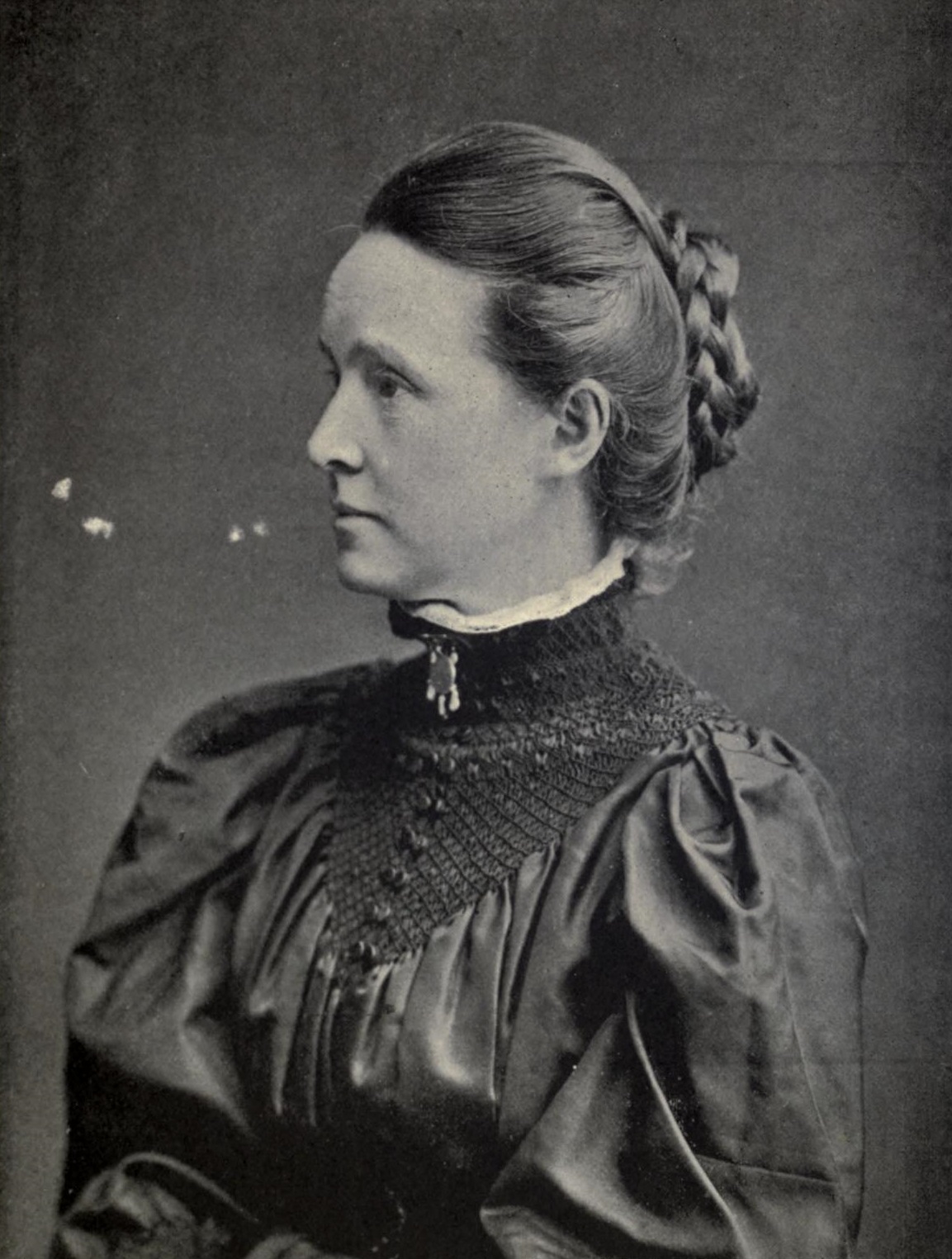 Black and white photo of Millicent Fawcett with hair up in a plaited coil on the back of her head, wearing high collared Edwardian dress. Photo taken approx 1897.