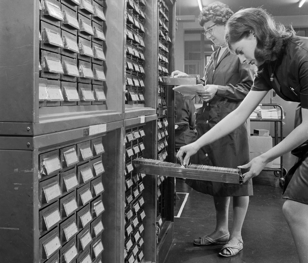 Women using the large card index cabinet in the premises of the medical mailing company in Ealing, 1960 - 1970