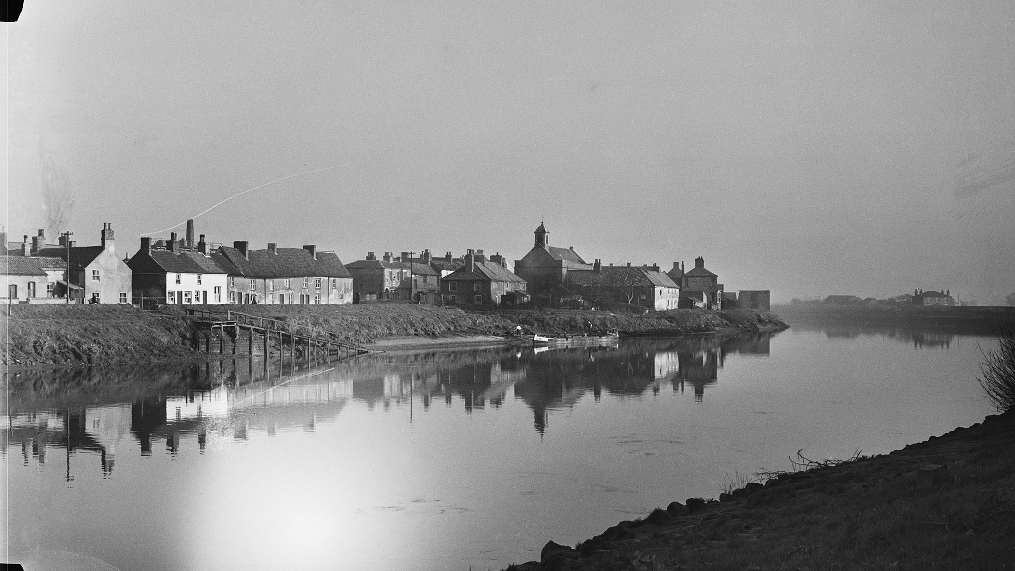 Black and white archive photograph of a townscape viewed across a river.
