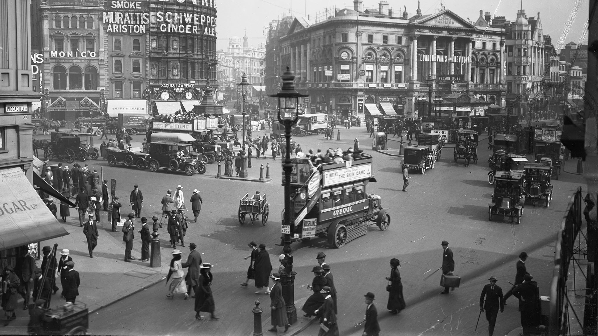 A busy street scene with pedestrians, buses and other vintage vehicles.