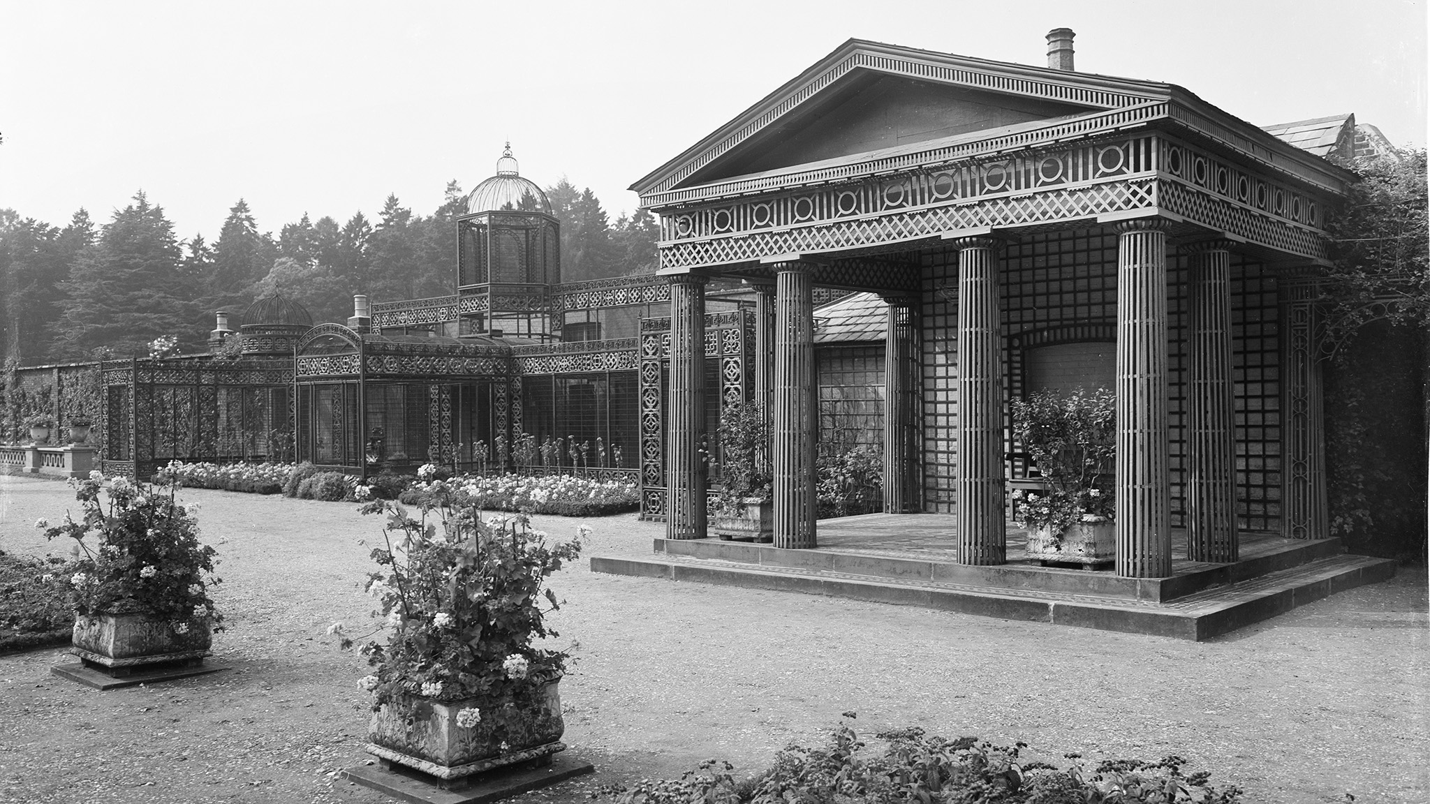 archive black and white photograph of a classical style colonnaded garden building and an elaborate wrought-iron aviary