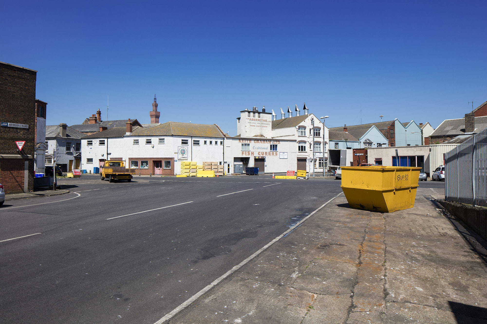 Photo shows a yellow skip on a pavememnt and historic buildings in the background revealing Grimsby's fishing heritage