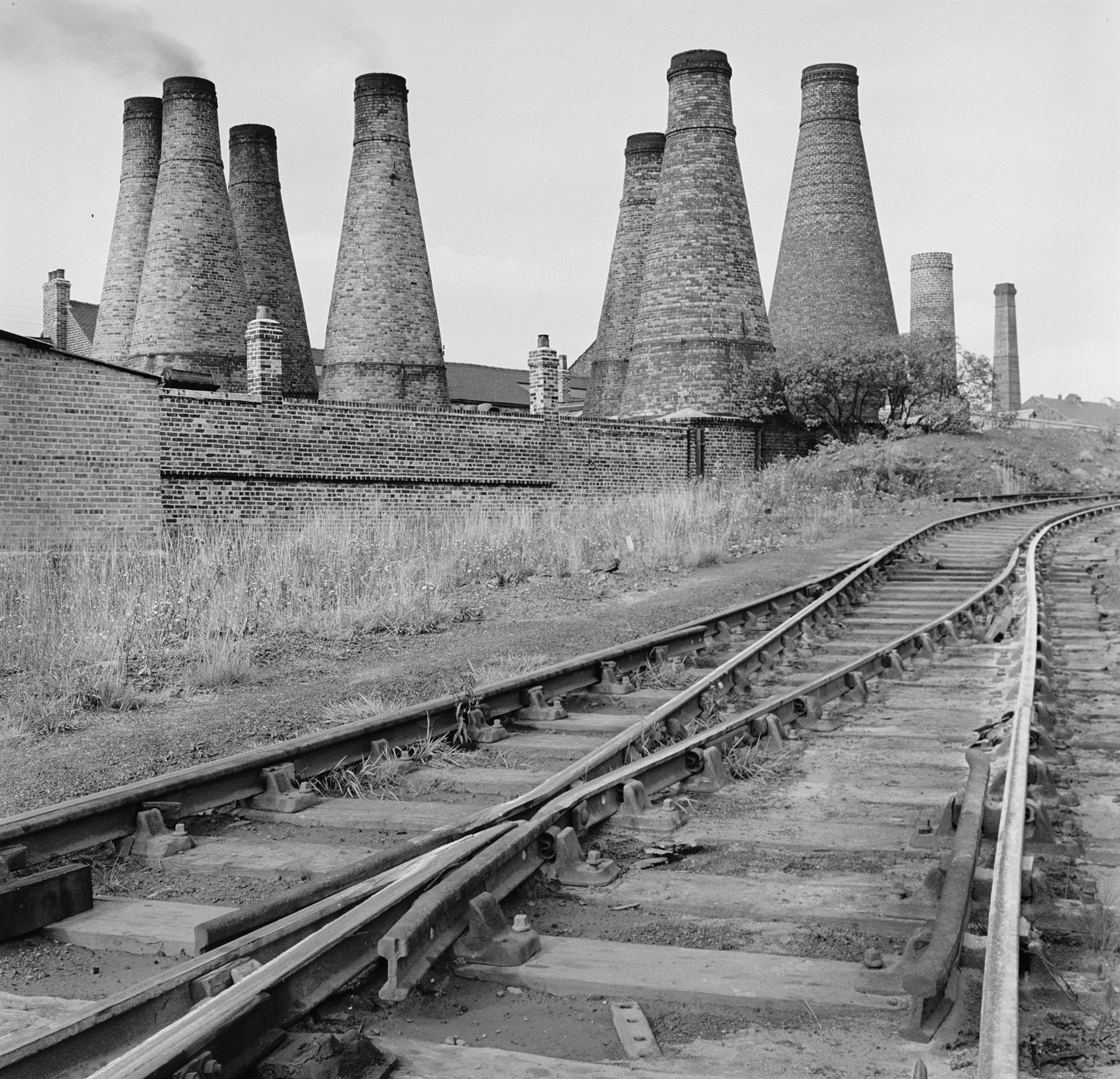 Black and white photo shows railway tracks in front of kiln chimneys