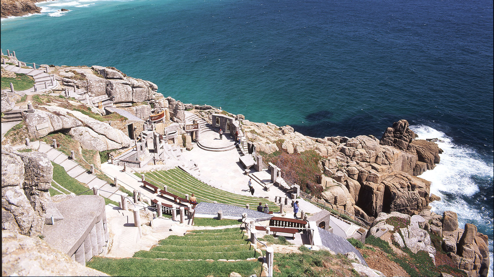 High view of Minack Theatre carved into cliff face with the sea in the background