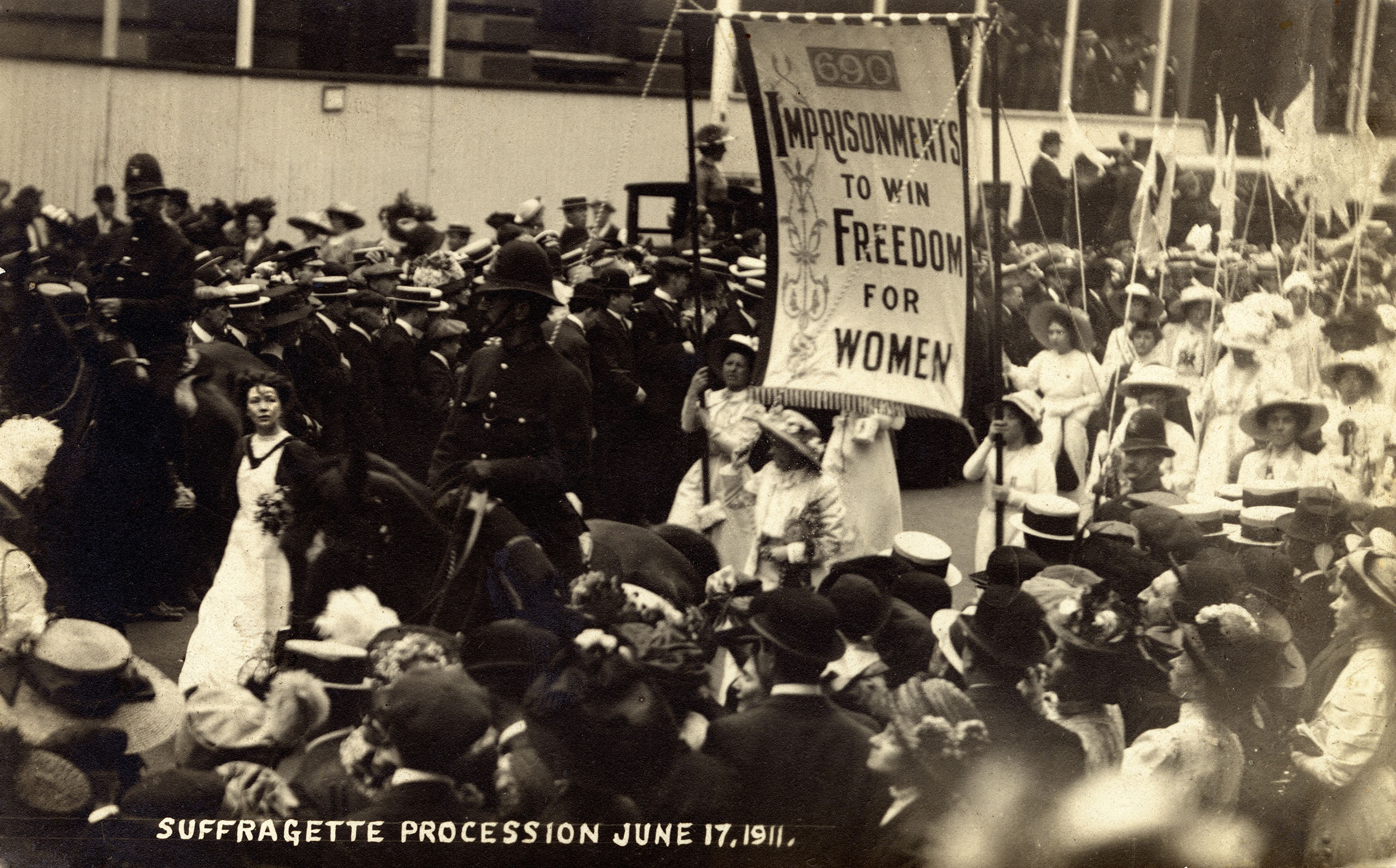 Black and white photo of suffragette procession 1911. Banner text reads: 690 imprisonments to win freedom for women
