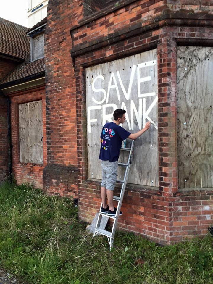 Josh Aitken-Dunkeld standing on a ladder painting SAVE FRANK on board