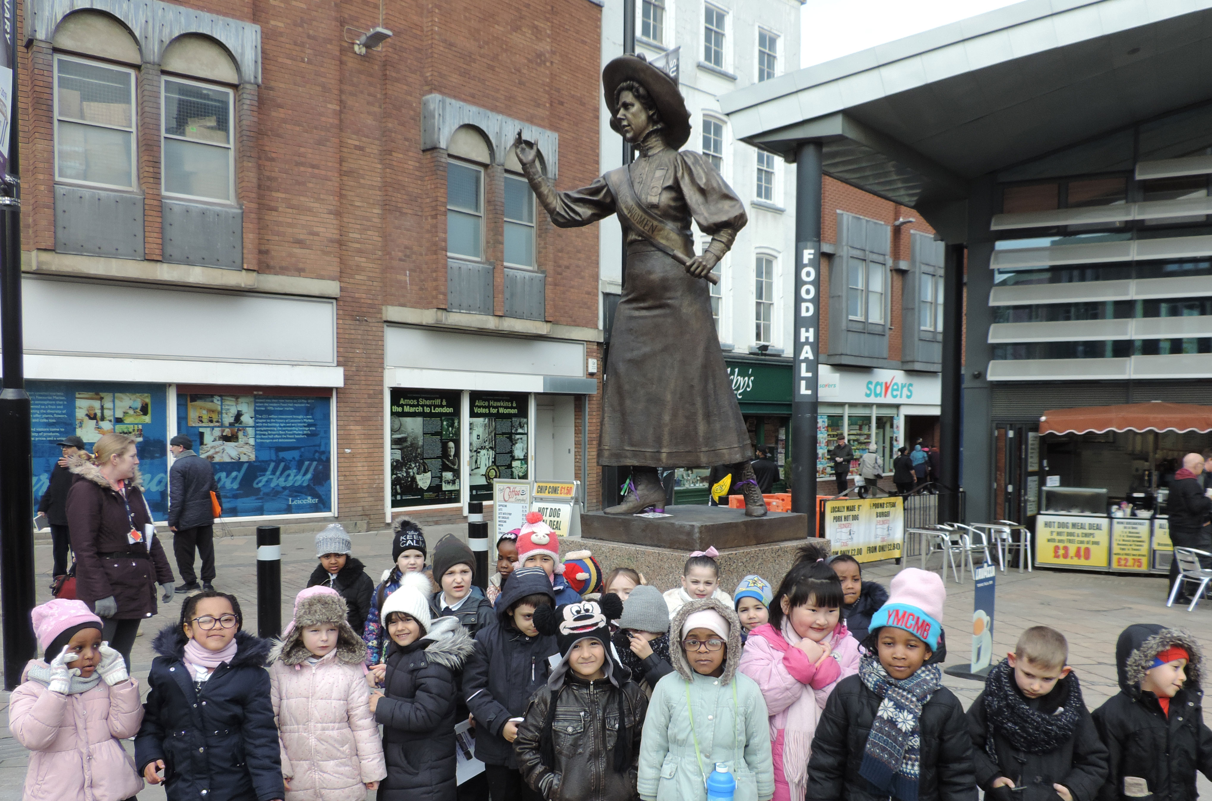 A group of about 20 Year 1 children posing for a group photo in front of Alice Hawkins statue in Leicester.