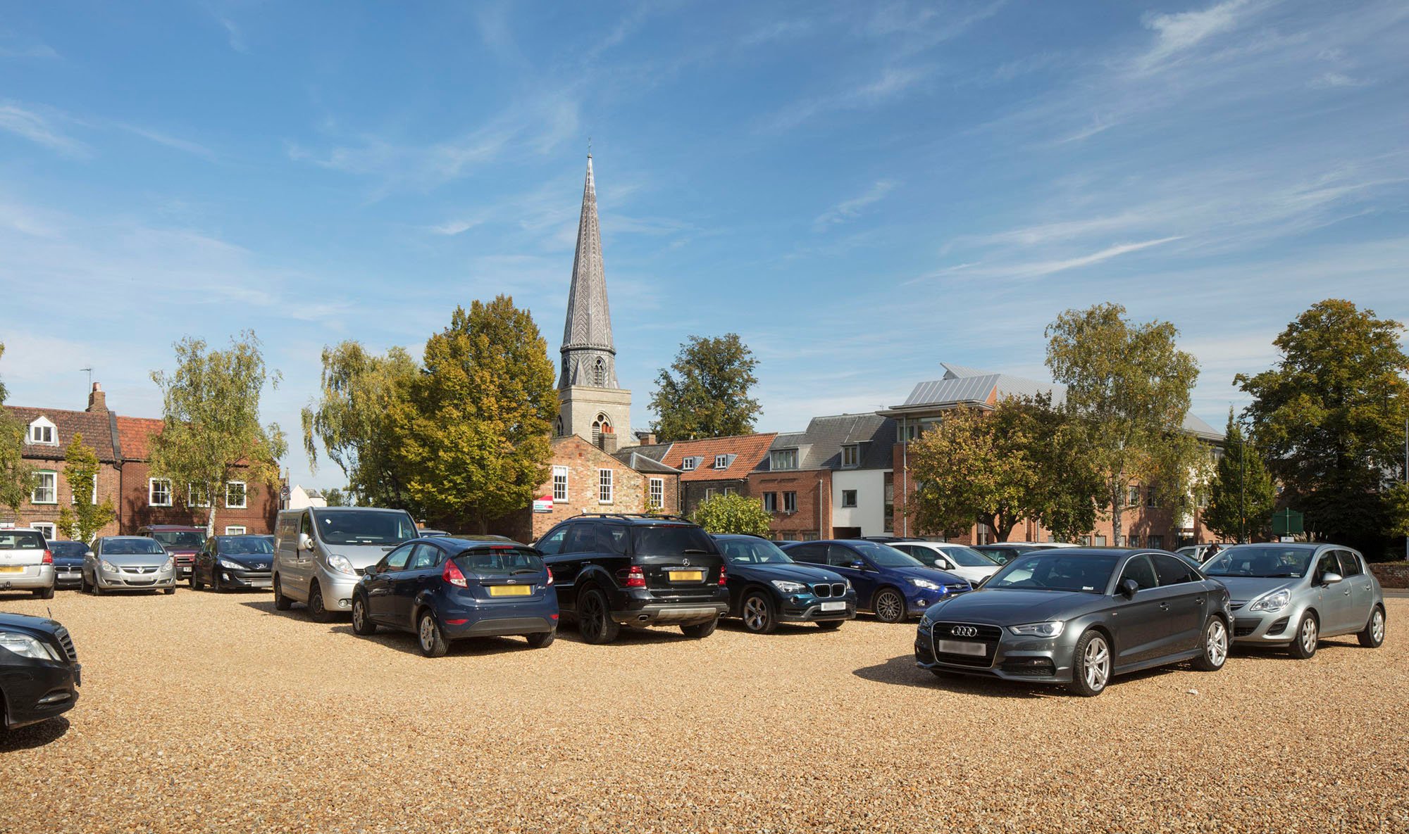 Cars parked in car park with church spire in background