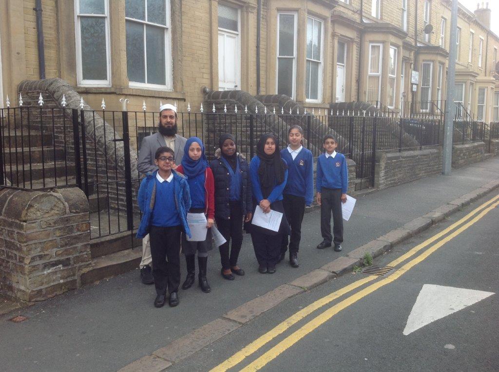 A group of six chool kids and their teacher standing in front of railings and stone built houses on Howard Street Bradford