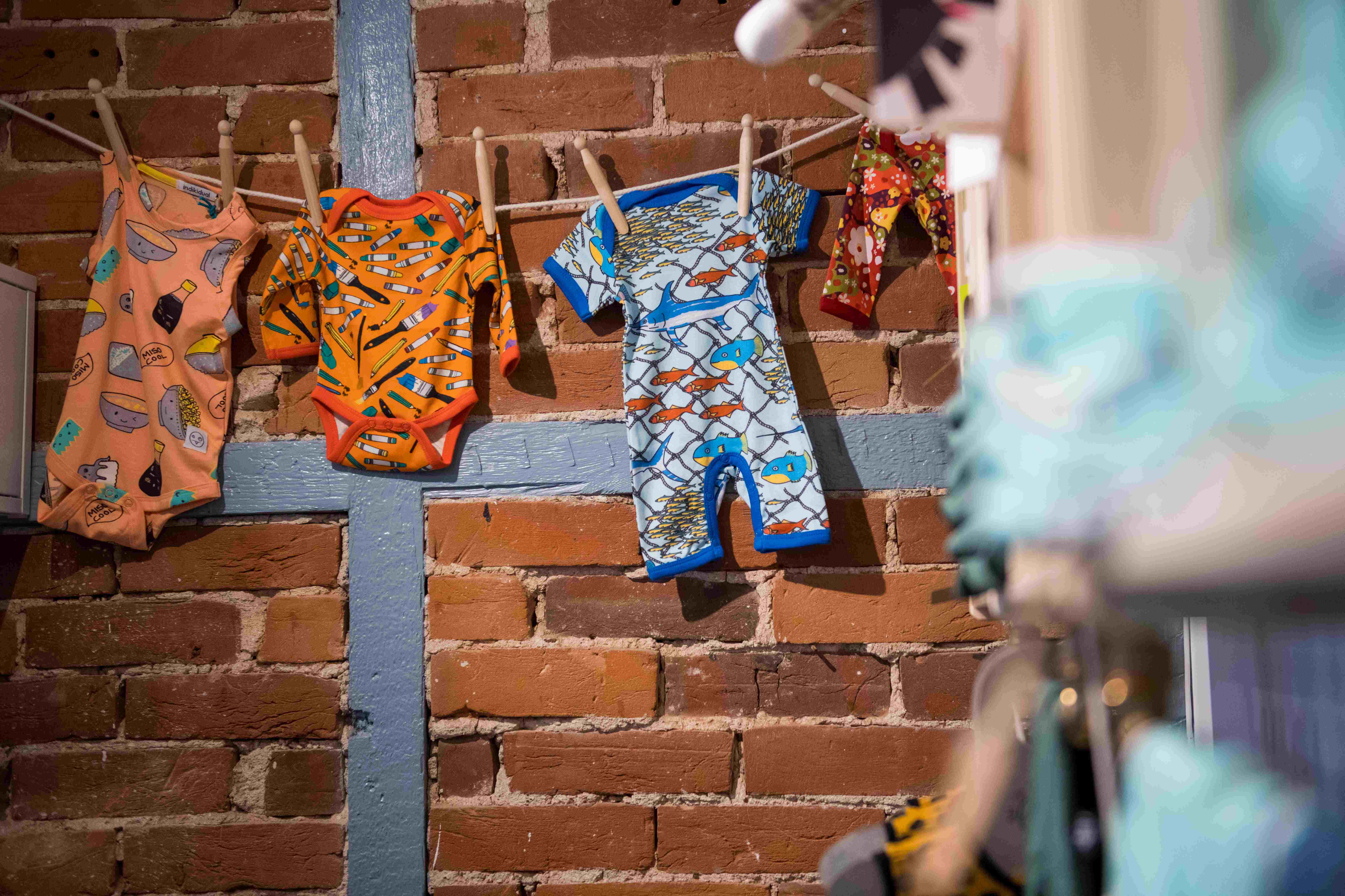 Colourful baby clothing displayed hanging on a washing line across the old brick wall of Moo Like a Monkey shop premises.