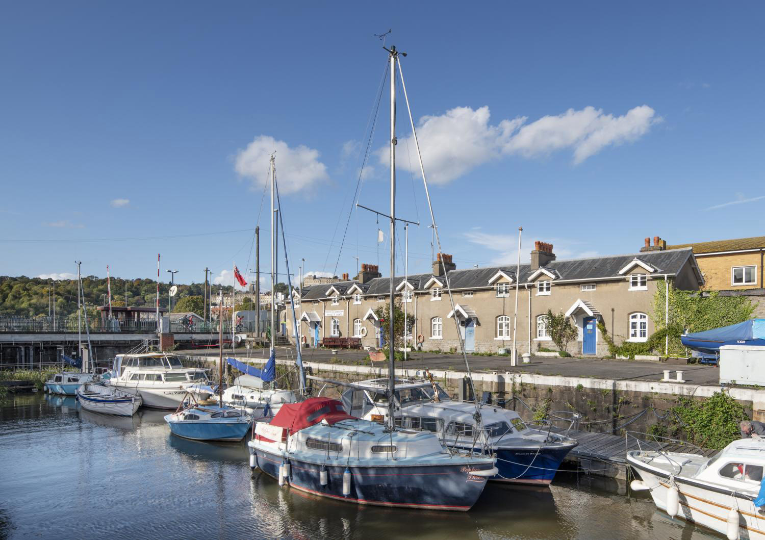 A photograph of a lock with small leisure boats in the foreground. There are historic lock structures on the quayside, including bollards, and cottages beyond.