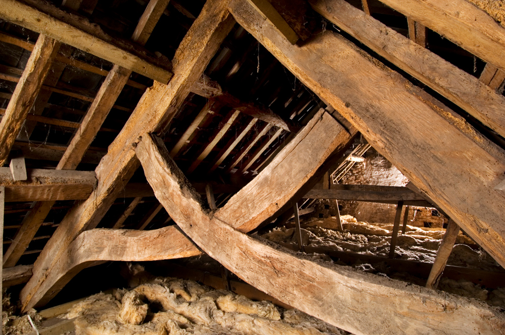 Interior of farmhouse loft showing old wooden beam structure and insulation.