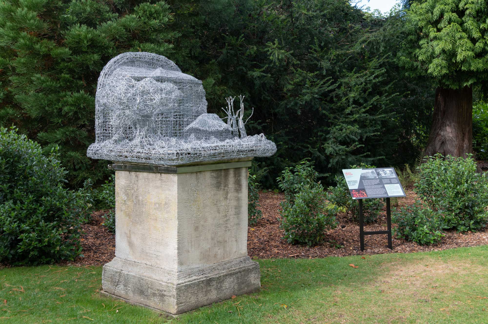 An installation comprising a wire sculpture of plantation structures, set on an existing stone plinth in a country house garden.