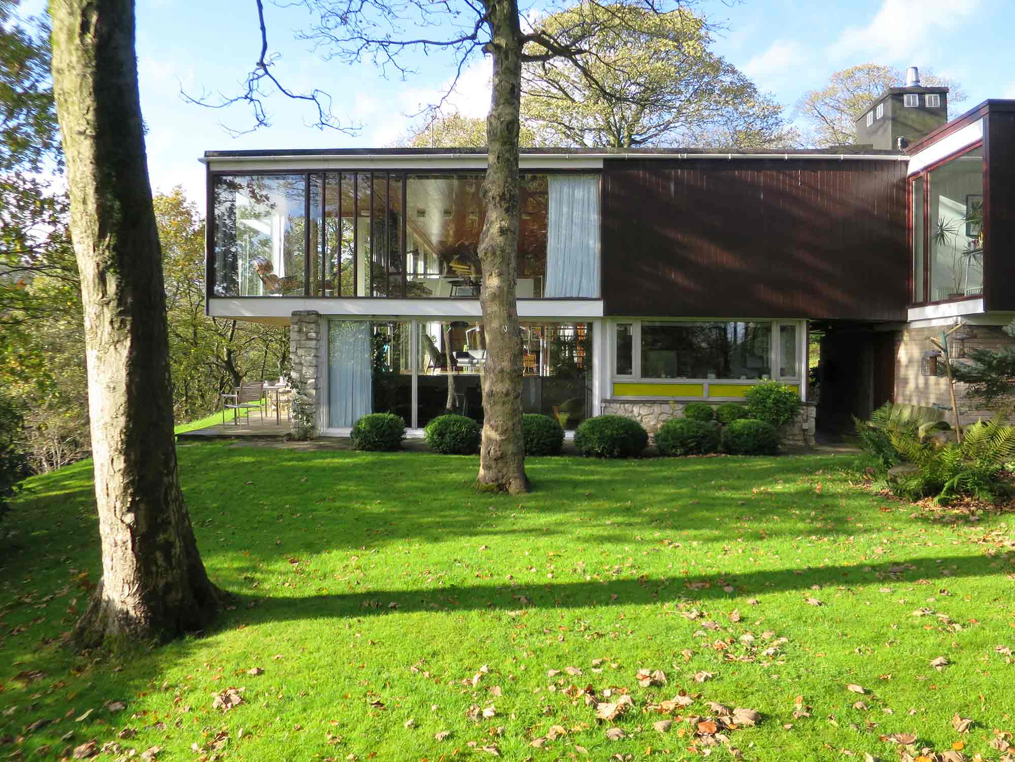 Flat-roofed modern house with top floor overhanging the lower floor surrounded by large trees