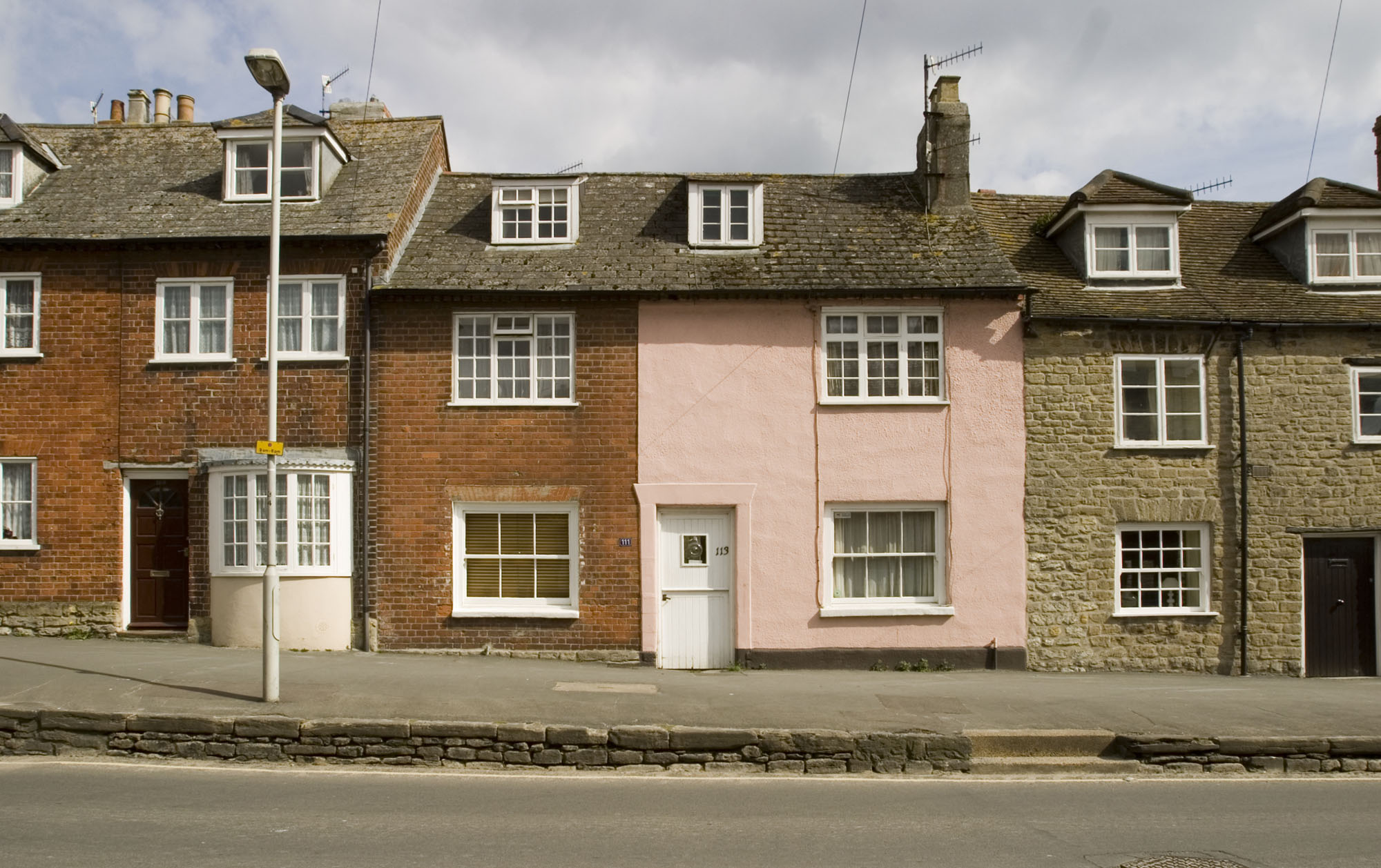 Three attached houses along a street, each with a different wall type. From left to right: brick, render and stone.