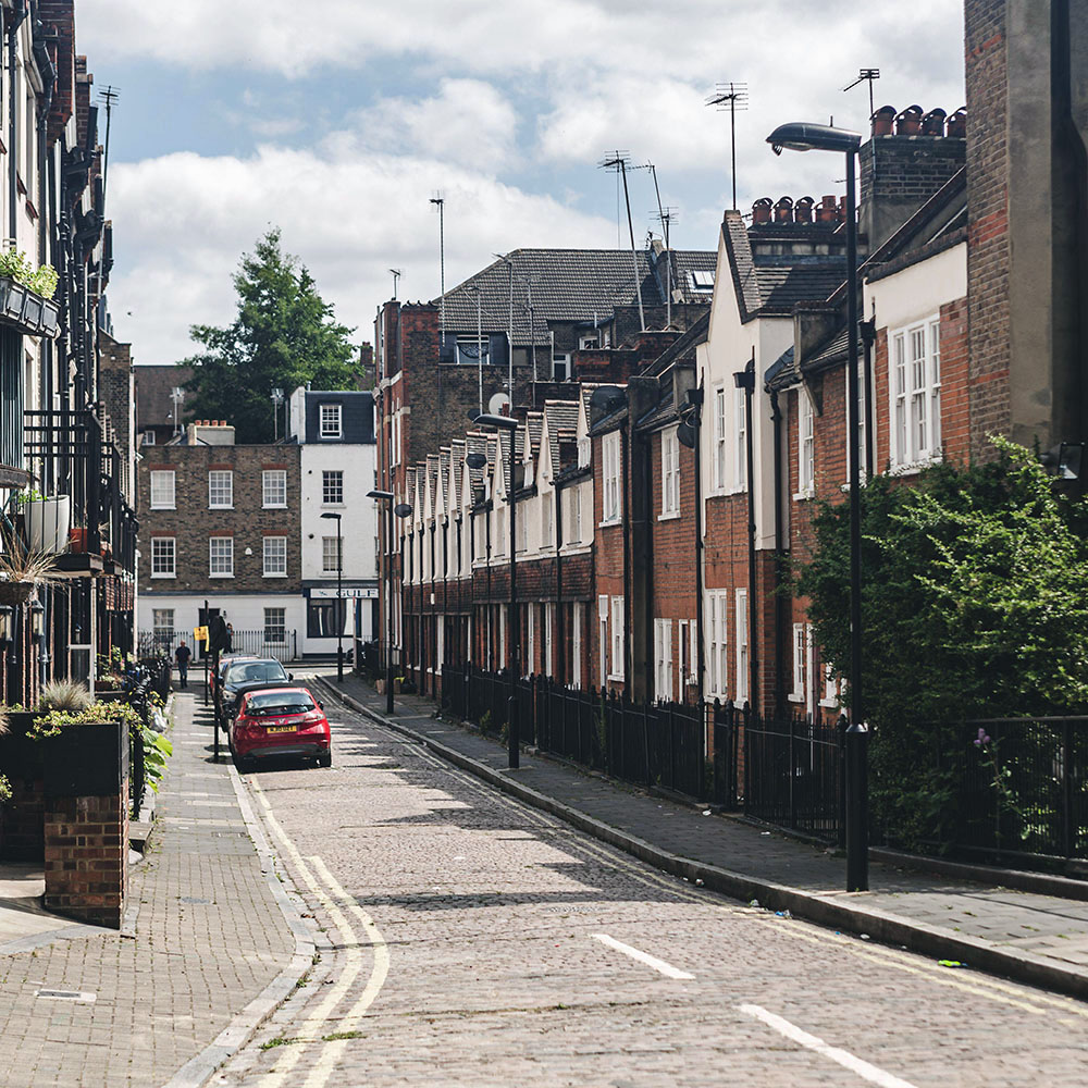 A narrow residential street in London, with brick, tile, and rendered townhouses. 