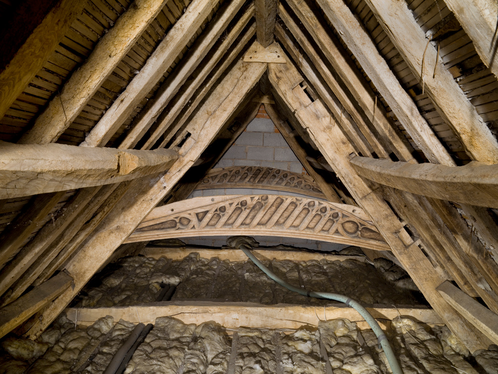 Interior of a farmhouse loft showing old wooden beams and loft insulation.