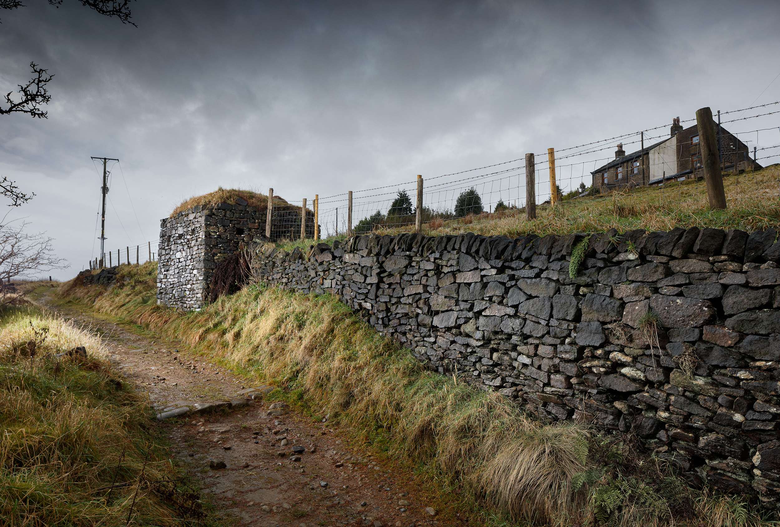 Dry stone wall and pillbox exterior walls and turfed roof giving the appearance of an agricultural vernacular building, camouflaging its real purpose.