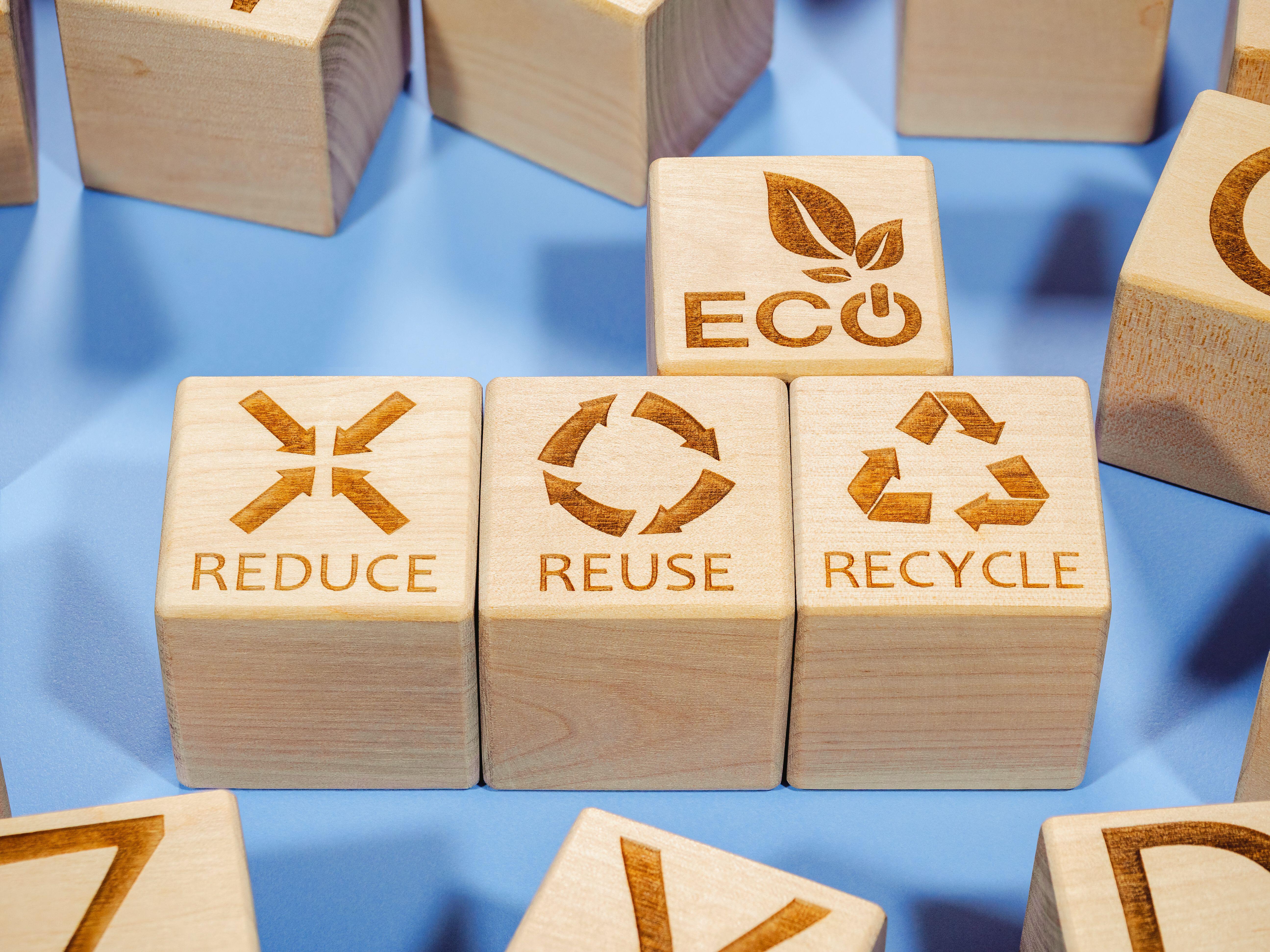 A symbolic depiction of a slogan aimed an encouraging carbon reduction and sustainability: three wooden building blocks are lined up to spell out "reduce" reuse and recycle; above these is a block labelled "Eco".