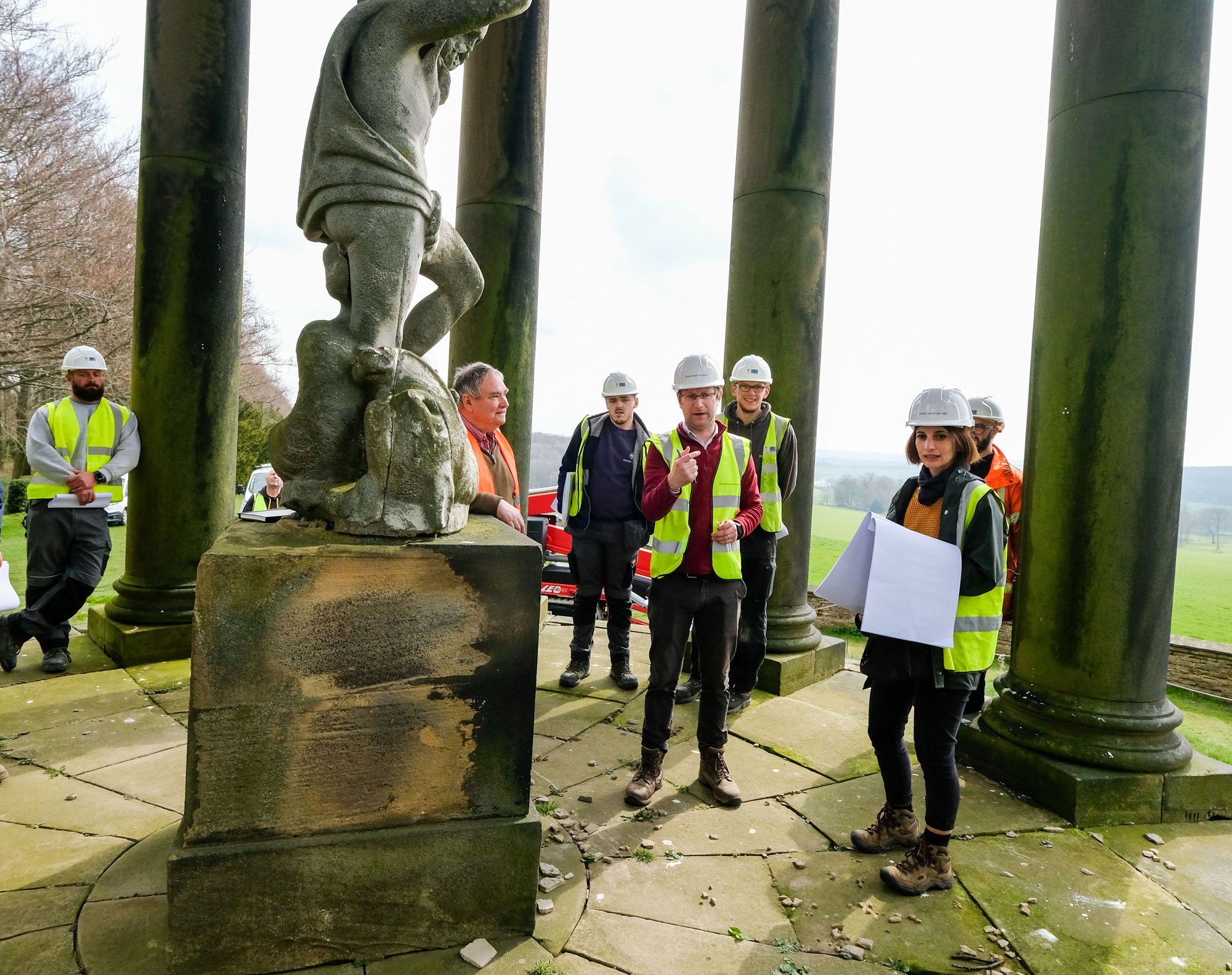 Group of people in hard hats and high-vis jackets visiting a historic site.