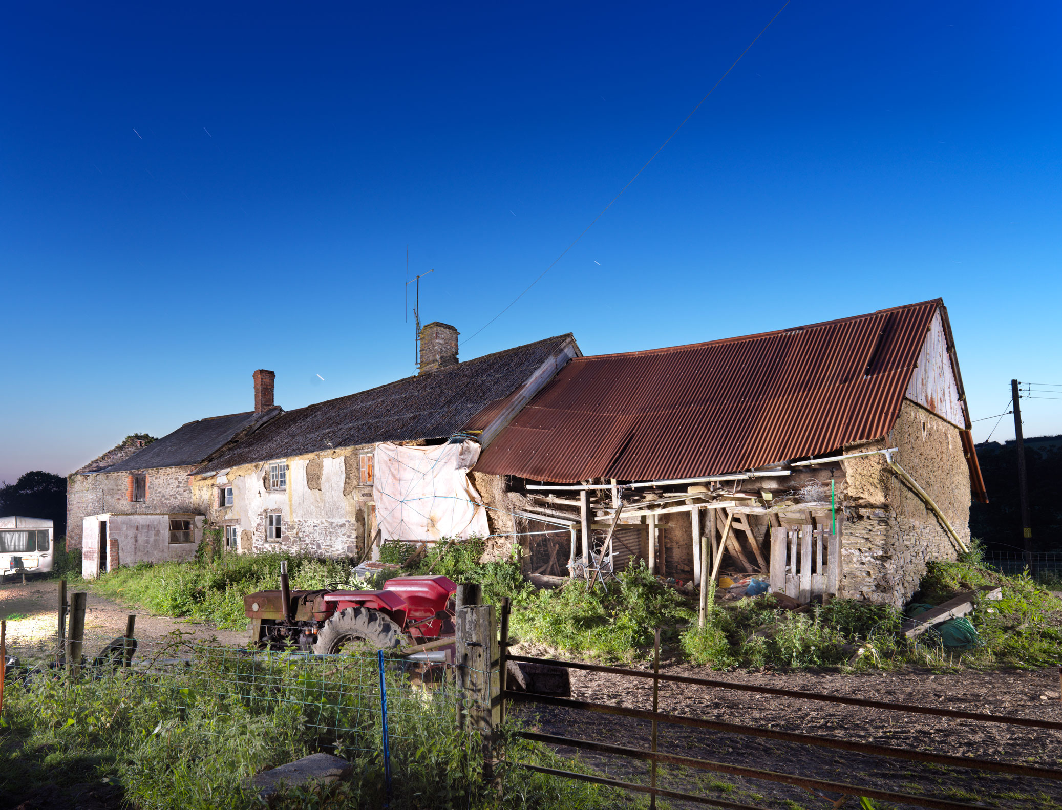 A farmhouse flanked by derelict outbuildings.
